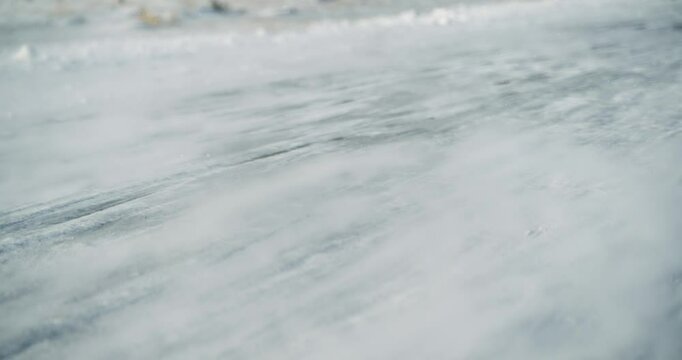 Field enveloped in snow during a cold winter day, as strong winds cause drifting snow and highlight the serene but harsh beauty of nature