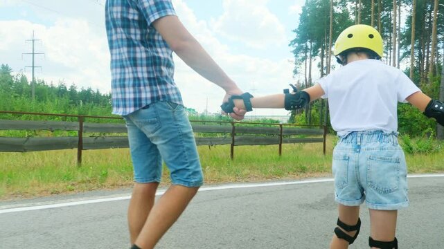 Child girl holding dad's hand, roller skating in the summer park.