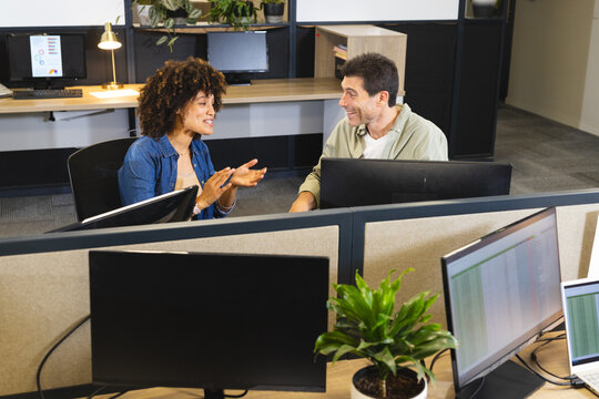 Collaborating Diverse coworkers sitting at cubicles in open-plan office, with computers and plants
