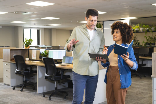 Discussing ideas Diverse coworkers standing in office, with blue notebook and tablet
