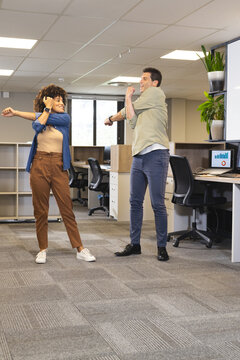 Diverse coworkers stretching arms across chests in open-plan office, with monitors and plants