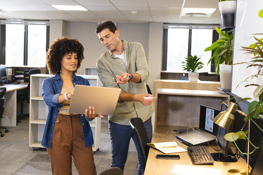 Collaborating Diverse coworkers reviewing data on laptop at open office, with colorful marker pens