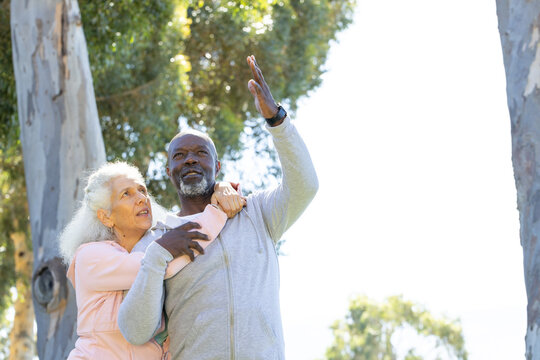 Stretching senior couple reaching toward sky in sunlit park, with smartwatch on man's wrist - Powered by Adobe