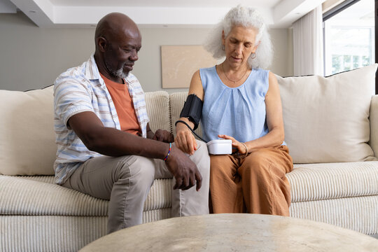 Measuring blood pressure Diverse senior couple sitting on sofa at home, with automatic monitor