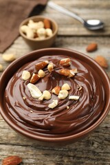 Delicious chocolate pudding with nuts in bowl on wooden table, closeup
