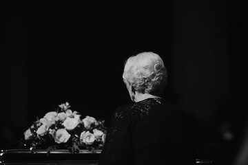 A solemn moment as a person mourns, looking towards a flower-adorned coffin. The image captures a scene of grief and remembrance