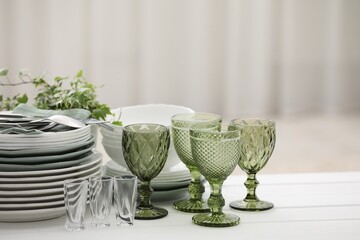 Clean glasses, plates, cutlery and green houseplant on white wooden table indoors