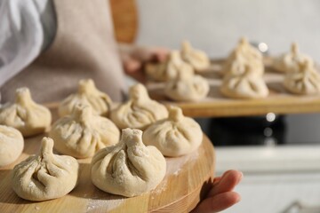 Woman with many uncooked khinkali in kitchen, closeup
