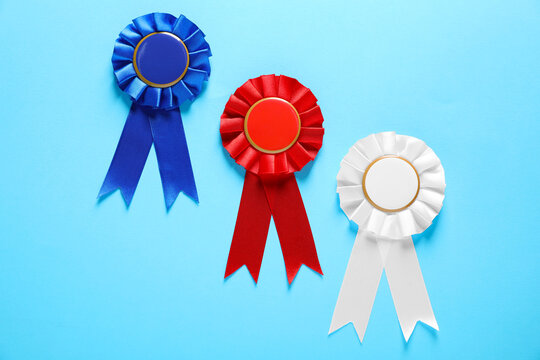 Colorful award ribbons on light blue background, flat lay