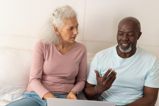 Senior couple sharing silver laptop in living room, reviewing documents together
