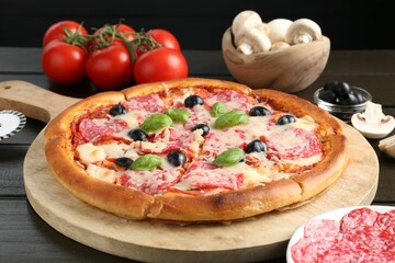Tasty pizza and ingredients on black wooden table, closeup
