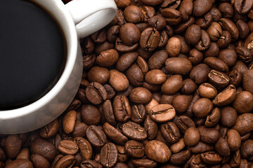 Textured background of fresh roasted coffee beans and a cup of coffee close-up