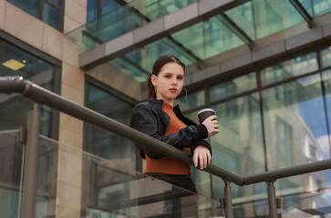 Girl with hot coffee against the background of a modern city building.