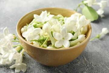 Beautiful jasmine flowers in bowl on grey table, closeup
