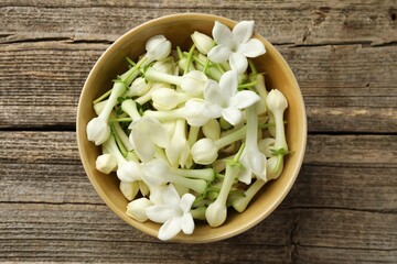Beautiful jasmine flowers in bowl on wooden table, top view