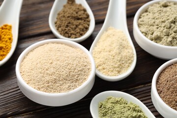 Different superfood powders in spoons and bowls on wooden table, closeup