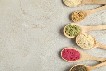 Different superfood powders in spoons on grey textured table, flat lay. Space for text