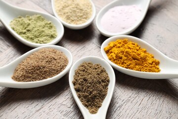 Different superfood powders in spoons on wooden table, closeup