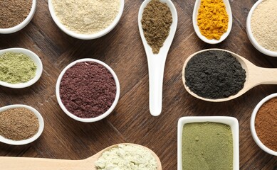 Different superfood powders in bowls and spoons on wooden table, flat lay
