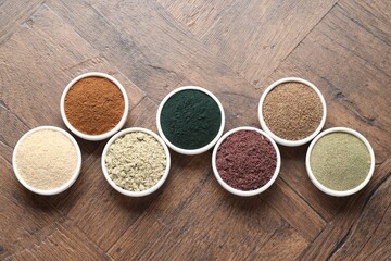 Different superfood powders in bowls on wooden table, flat lay