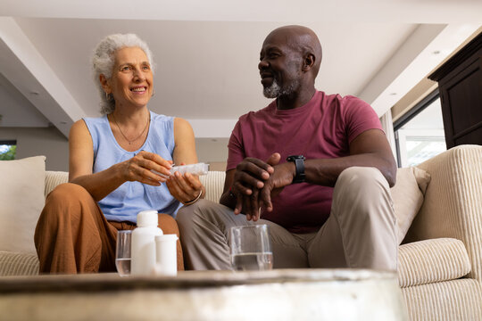 Sorting diverse senior couple managing pill bottles in living room, with pill organizer