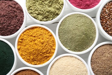 Different superfood powders in bowls on white wooden table, flat lay