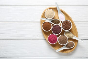 Different superfoods in bowls and spoons on white wooden table, top view. Space for text