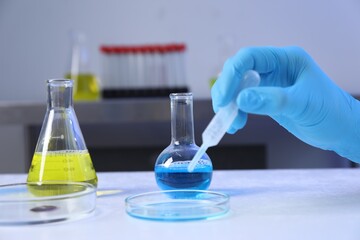 Scientist taking sample with pipette out of Petri dish at table in laboratory, closeup