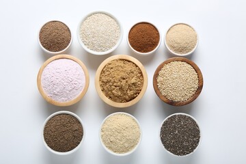 Different superfood powders in bowls on white background, flat lay