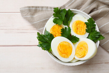 Boiled eggs and parsley in bowl on wooden table, top view. Space for text