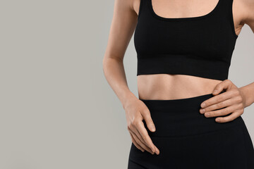 Beautiful woman with flat belly on gray background, closeup. Space for text