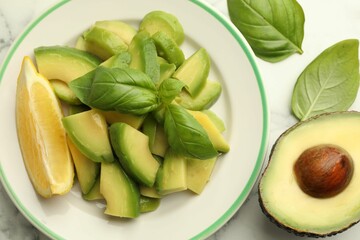 Tasty ripe green avocados, basil and lemon on white marble table, flat lay