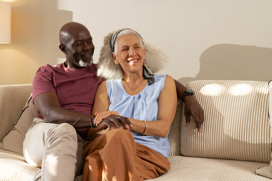 Smiling senior couple sitting on beige sofa in living room, with glowing floor lamp and smartwatch