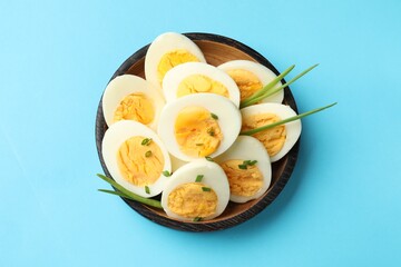 Halves of hard boiled eggs with green onions on light blue background, top view