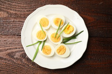Halves of hard boiled eggs with green onions on wooden table, top view