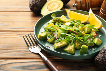 Tasty cut avocados with arugula, lemon and dressing on wooden table, closeup
