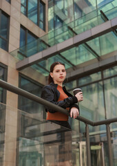 Girl with hot coffee against the background of a modern city building.