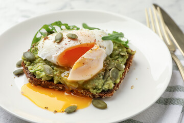 Delicious sandwich with avocado, poached egg, arugula and pumpkin on table, closeup