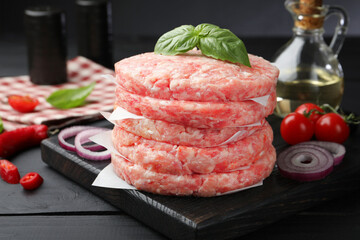 Fresh raw patties for burger, spices and tomatoes on black wooden table, closeup