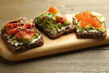 Different delicious avocado sandwiches on wooden table, closeup