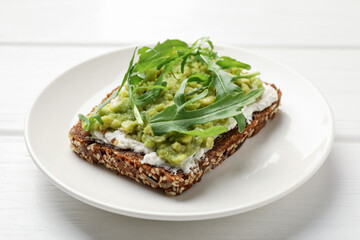 Delicious sandwich with avocado, cream cheese and arugula on white wooden table, closeup