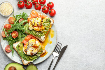Delicious sandwiches with avocado, poached egg and salmon served on gray table, flat lay. Space for text