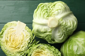 Fresh whole and cut cabbages on green wooden table, flat lay