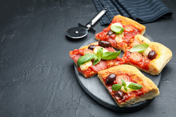 Pieces of tasty homemade pizza and cutter on black table, closeup. Space for text