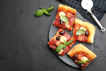 Pieces of tasty homemade pizza and cutter on black table, flat lay. Space for text