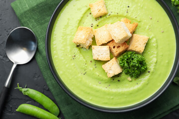 Tasty pea cream soup with croutons and broccoli served on black table, flat lay