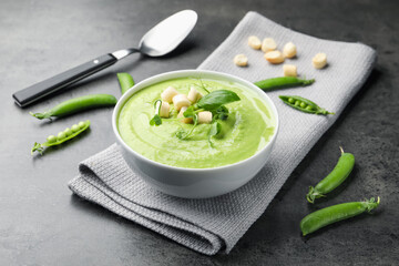 Tasty pea cream soup with croutons, basil and microgreens served on grey table