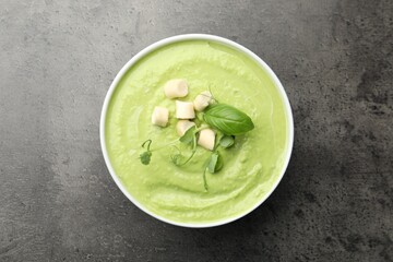 Tasty pea cream soup with croutons, basil and microgreens on grey table, top view