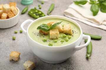 Tasty pea cream soup with croutons and basil served on grey table, closeup