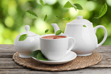 Green tea leaves flying above hot beverage on wooden table outdoors